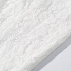 White lace fabric close-up with dense floral motifs across the skirt