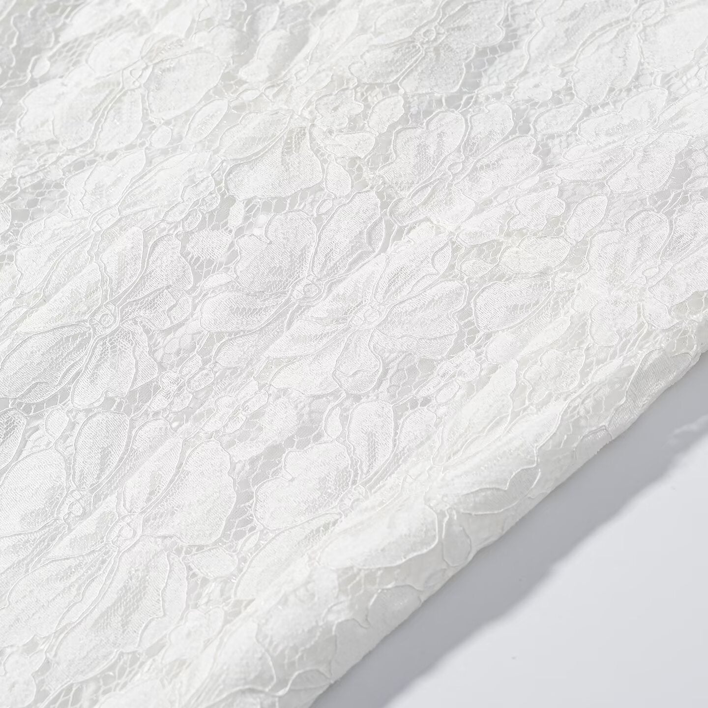 White lace fabric close-up with dense floral motifs across the skirt