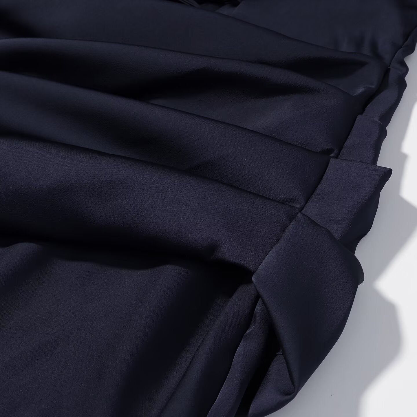Navy blue pleated fabric with diagonal drape and stitched seam on skirt