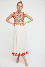 Women’s sleeveless floral dress with red patterned bodice, white skirt, red pom tassel hem.