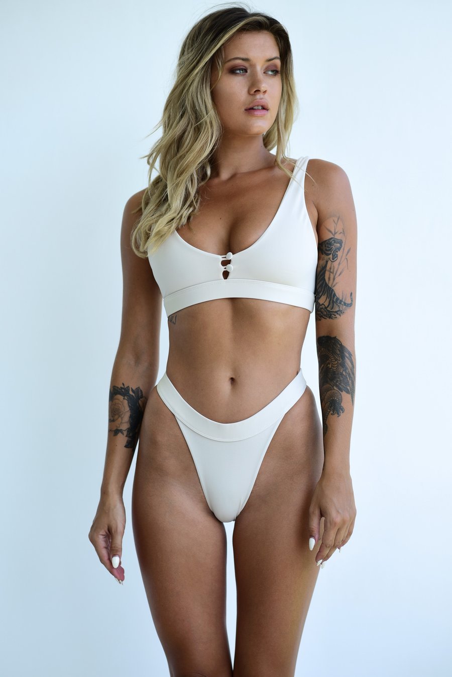 White one-piece swimwear with scoop neckline, high-cut bottom, and center ring clasp