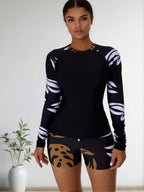 Black long-sleeve rash guard with white leaf sleeve pattern and tan abstract boy shorts