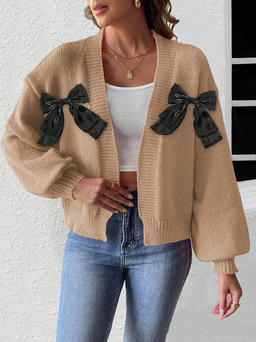 Beige knit cardigan with black shoulder ribbon bows and ribbed open front cuffs.