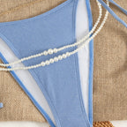 Blue bikini one-piece with pearl strand across front and slim high-cut tie sides