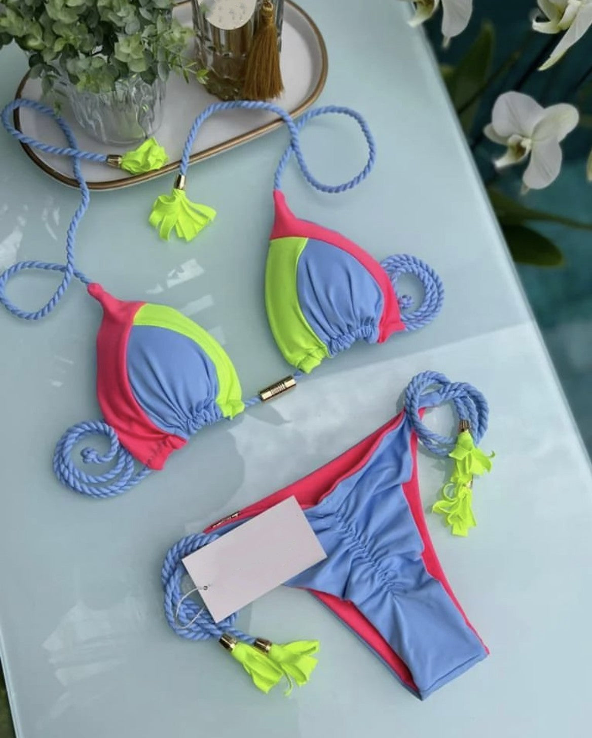 Patchwork bikini set flat lay: blue triangle top with neon green tassels and string ties