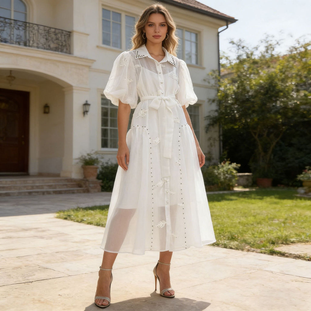 White maxi dress with puff sleeves, button front, lace trim, and tied waist belt