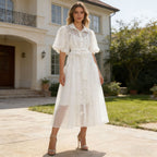 White maxi dress with puff sleeves, button front, lace trim, and tied waist belt