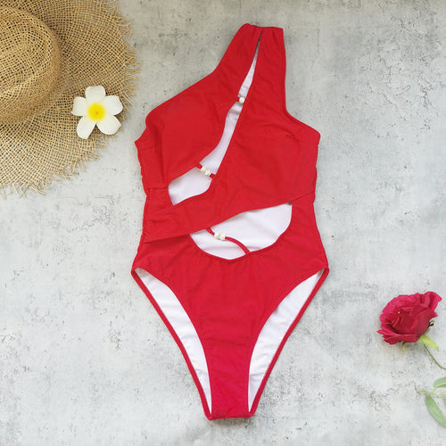 Red one-piece swimsuit with high-cut legs, one-shoulder drape, and white bead details