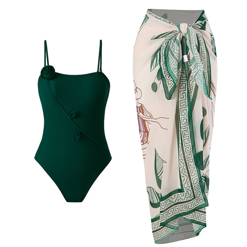 One-piece swimsuit in dark green with thin straps, paired with cream leaf wrap skirt