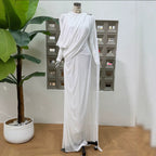 White pleated formal dress with long sleeves, diagonal drape detail, flowing maxi skirt