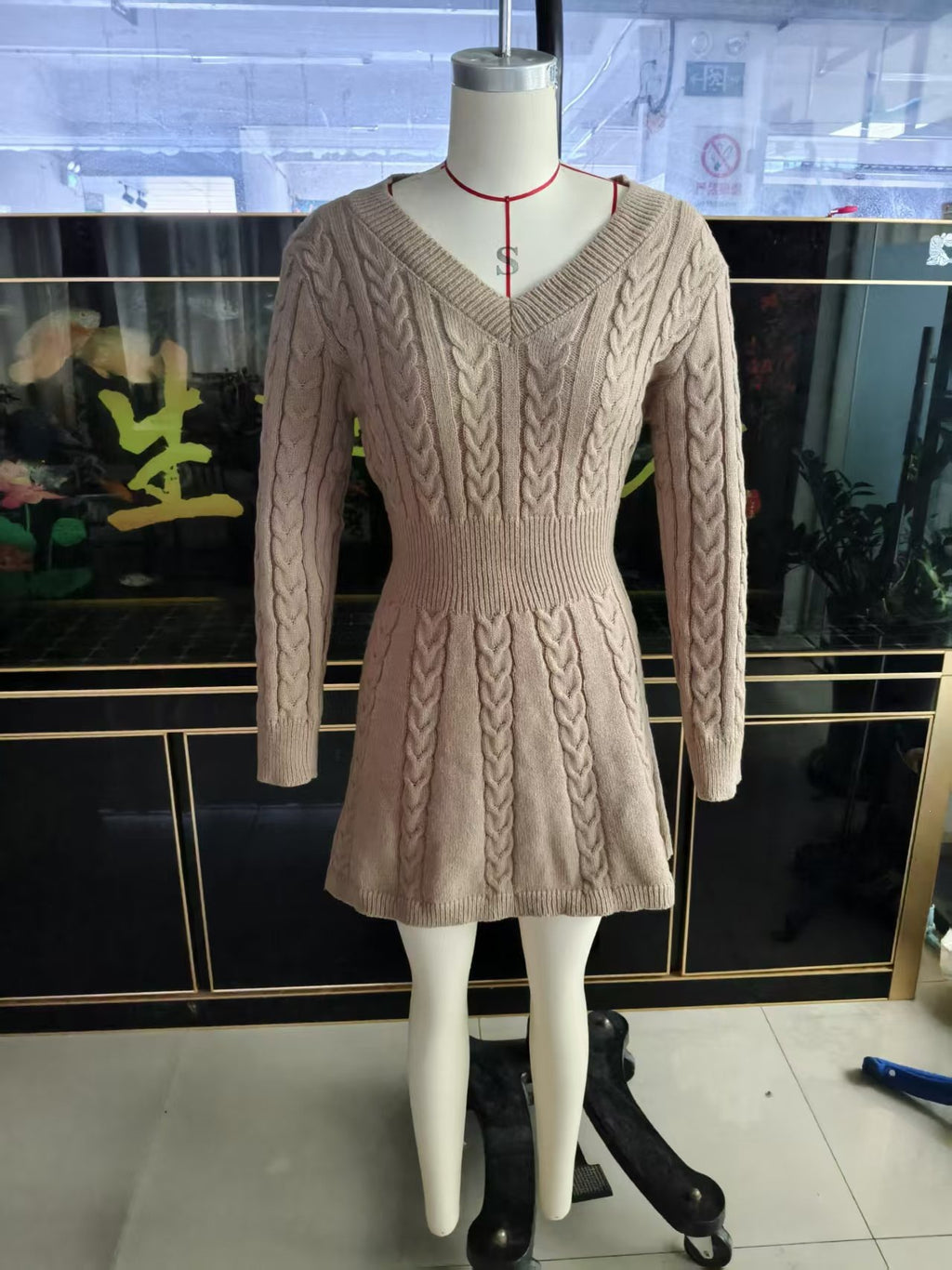 Beige knit V-neck dress on mannequin with long sleeves and cable pattern