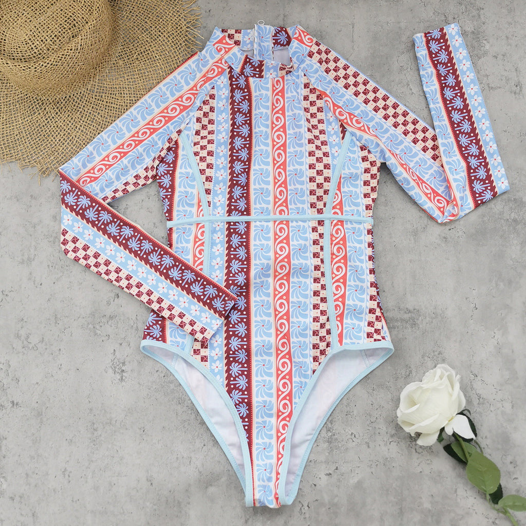 One-piece swimwear flat lay, long sleeves, high neck, light blue multi print with red accents