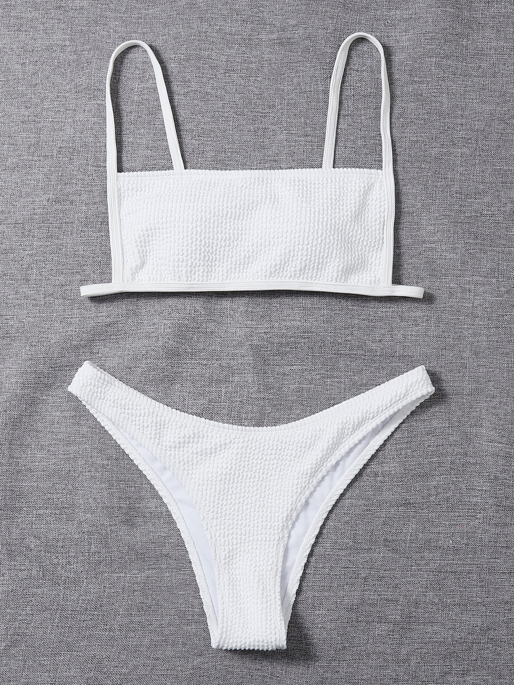 White textured bikini set laid flat: bandeau top with thin straps and low-rise briefs
