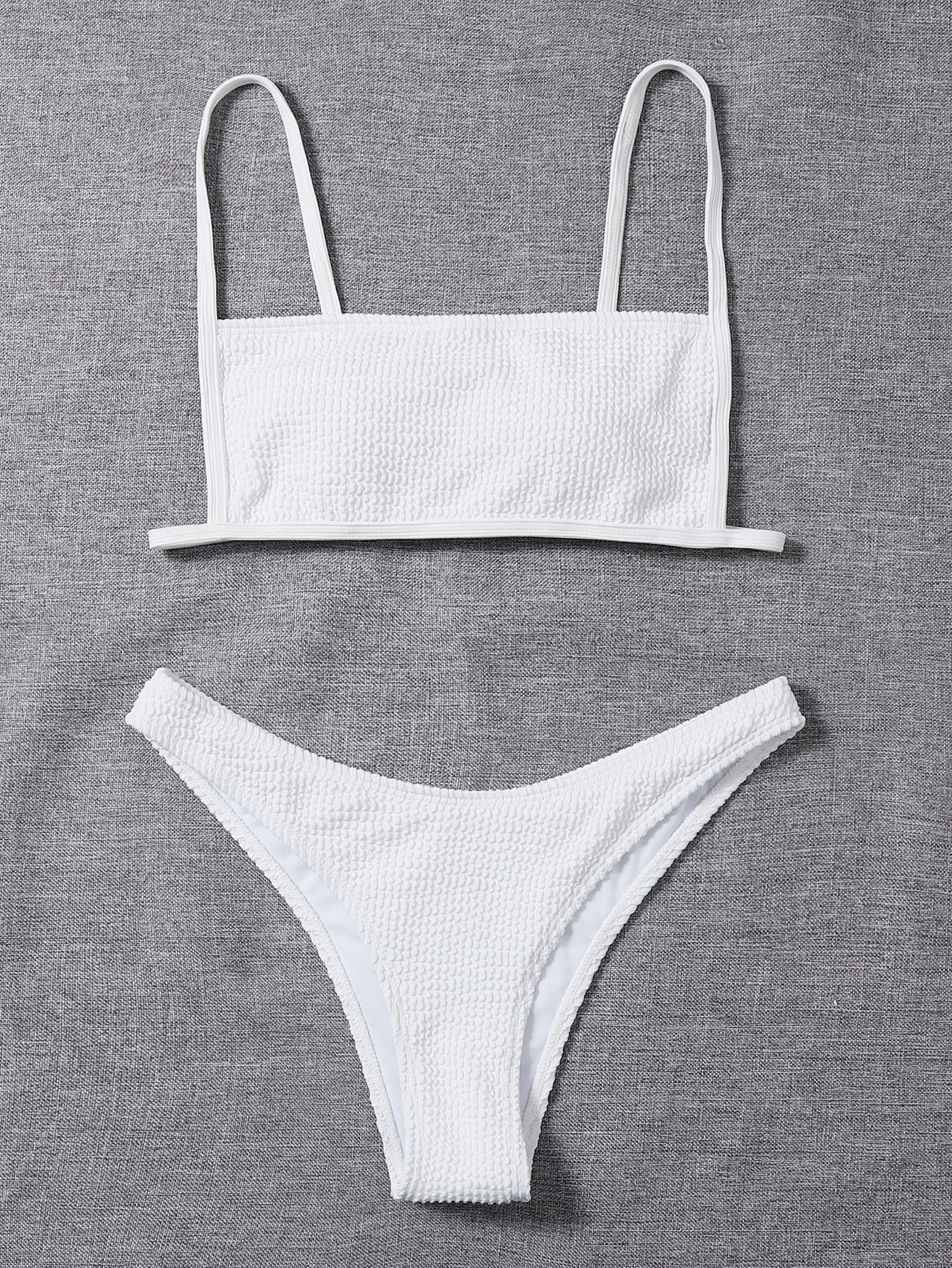 White textured bikini set laid flat: bandeau top with thin straps and low-rise briefs
